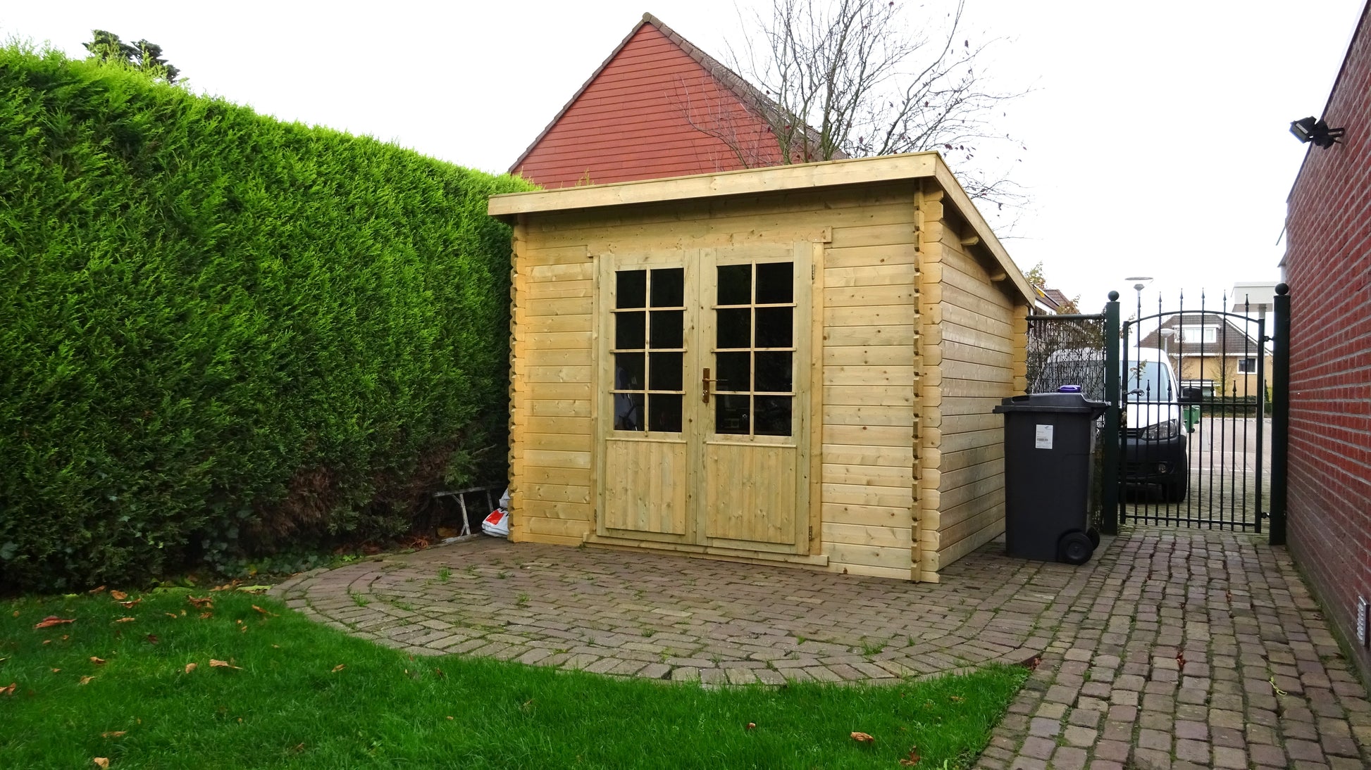 Licht houten tuinhuis Interflex 3030L op betonnen plaat in groene tuin met bomen